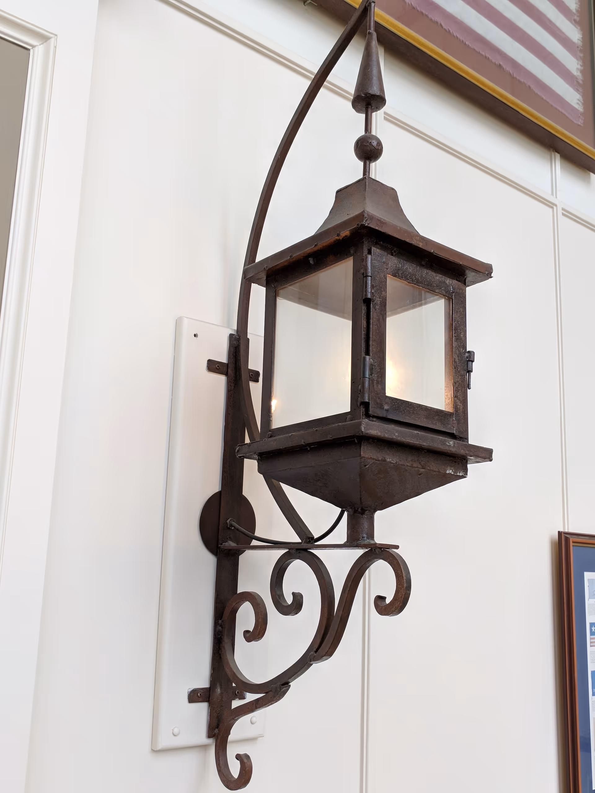 Ornate wrought-iron lantern sconce mounted on a white exterior wall.