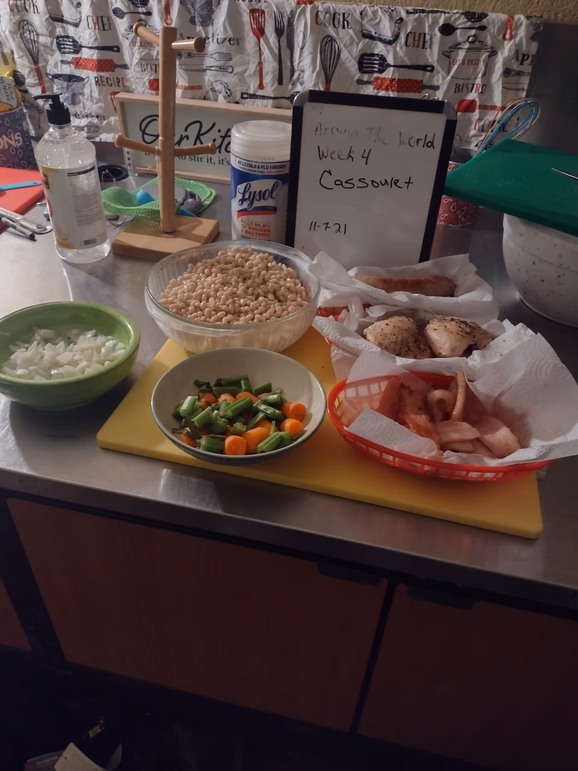 Kitchen counter with bowls of chopped vegetables, chickpeas, and meat, plus a whiteboard.