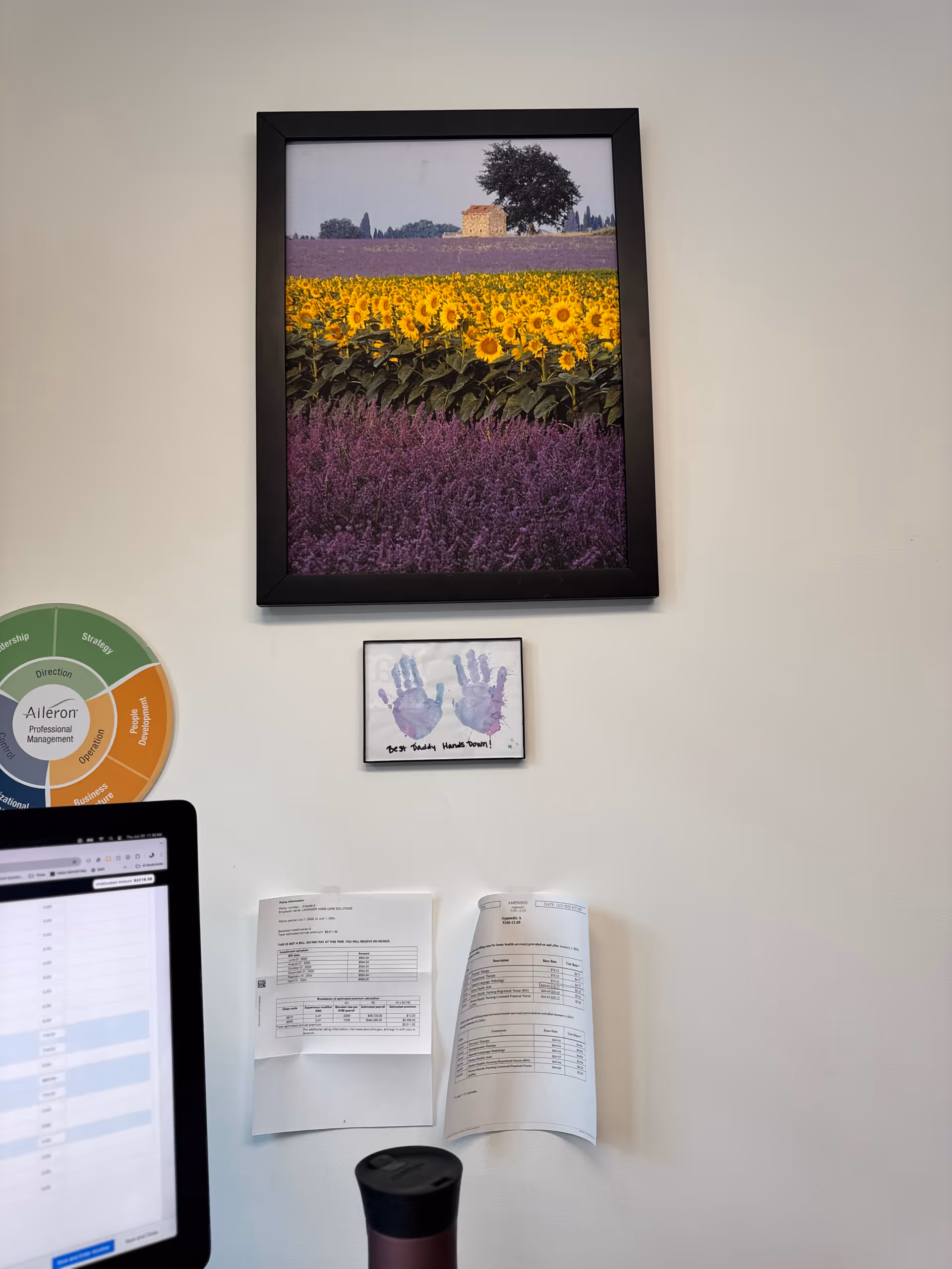 Interior wall of an office with framed flowers, scattered papers, and a computer monitor.