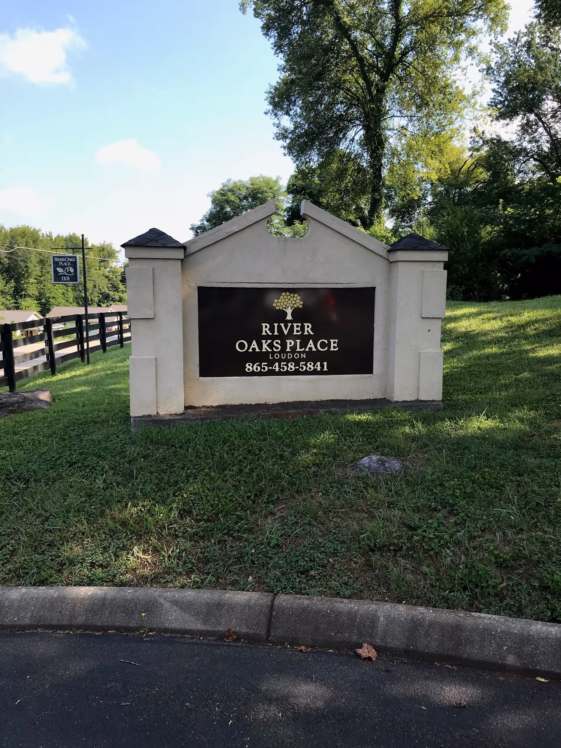 Stone entrance sign reading River Oaks Place Loudon amid trees and grass.