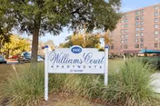 Williams Court Apts sign stands among landscaping in front of a brick building.