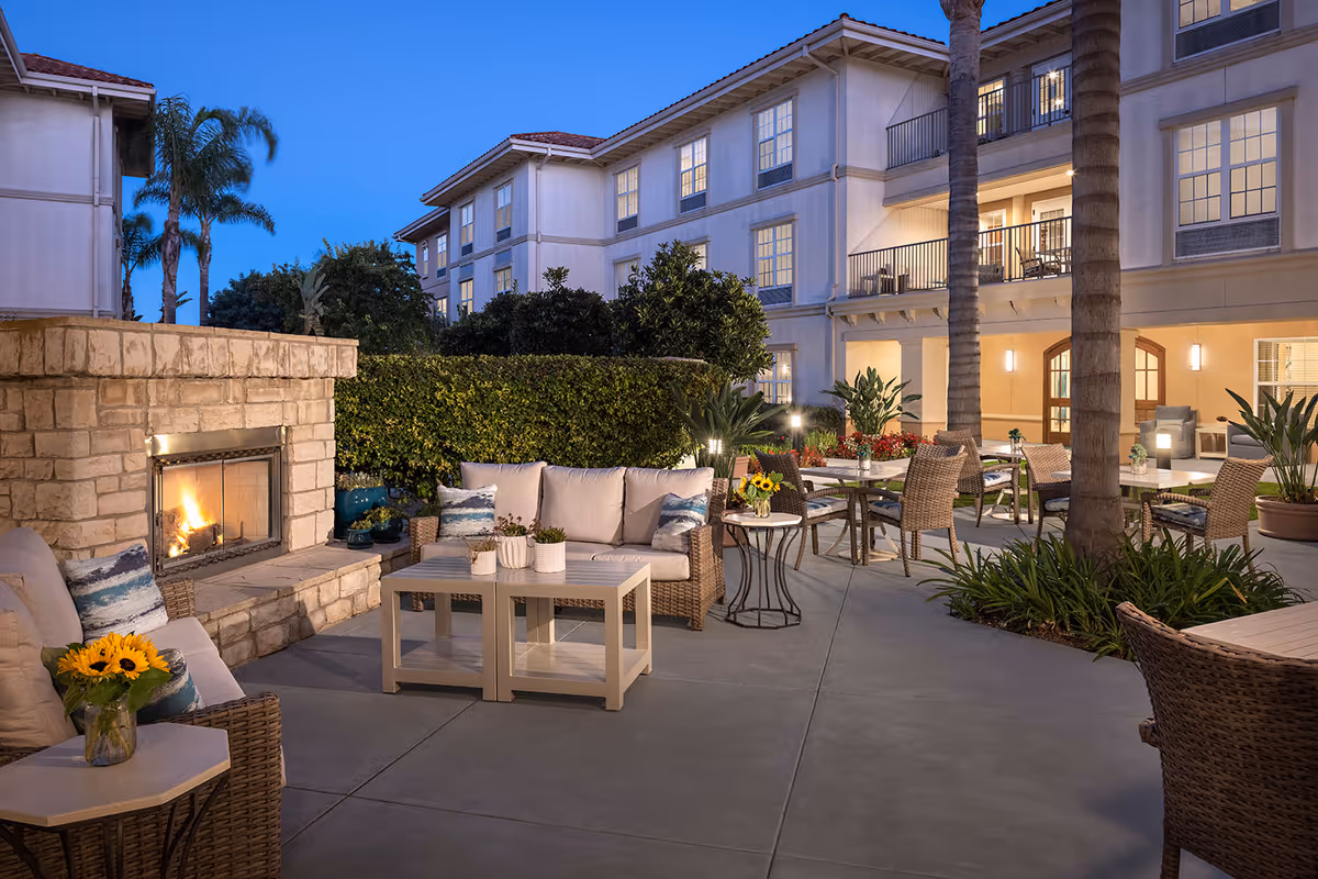 Outdoor patio with a stone fireplace, cushioned seating, and dining tables in front of a building.