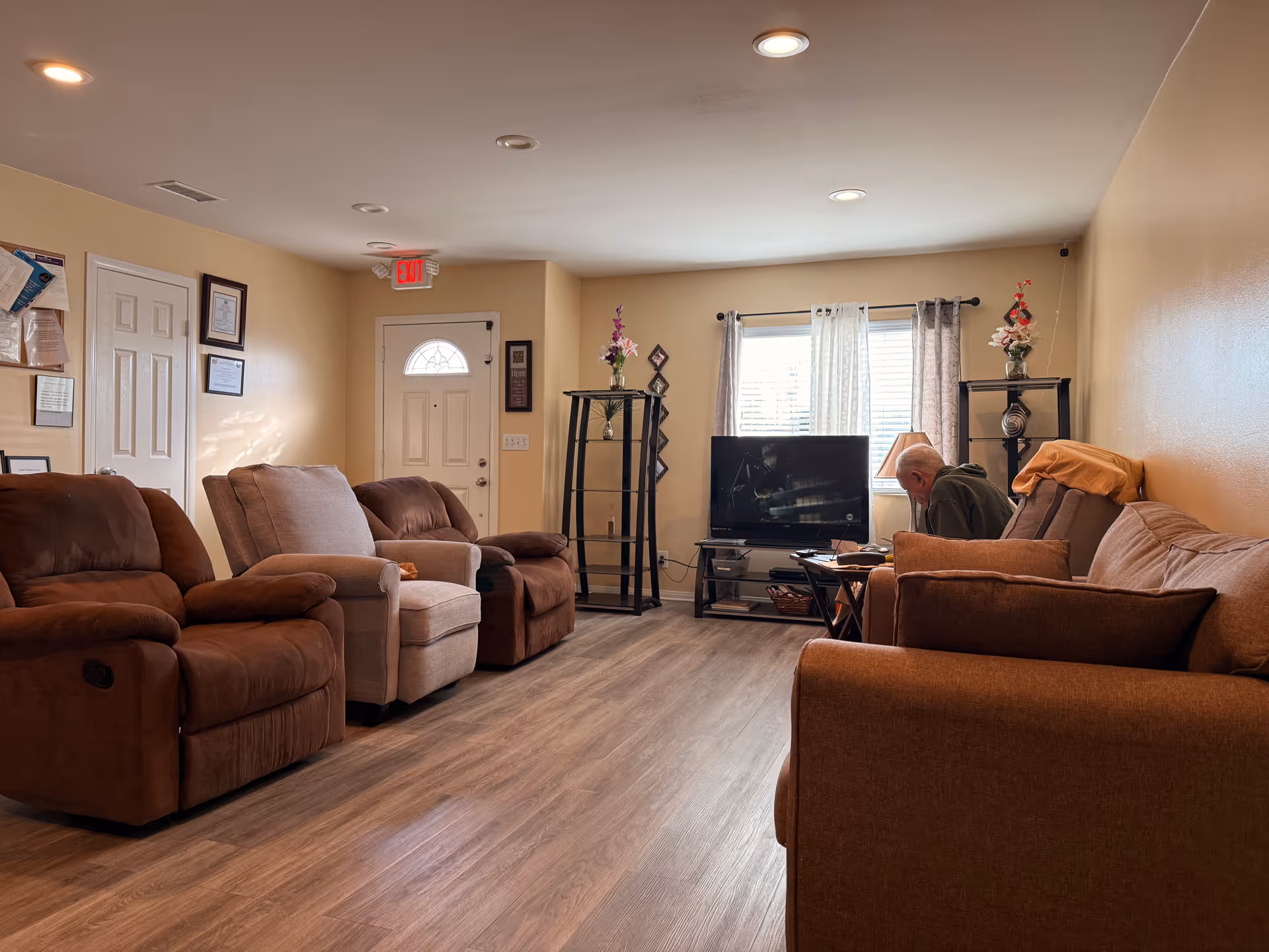 Cozy living room with brown recliners, a TV, shelves, and a seated resident.