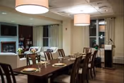 Indoor dining room with a long table set with plates, glasses, and chairs.
