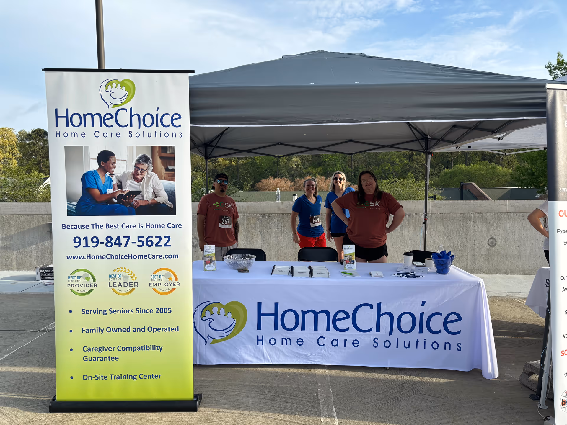 Outdoor promotional booth for HomeChoice Home Care Solutions with banner, table, and staff.