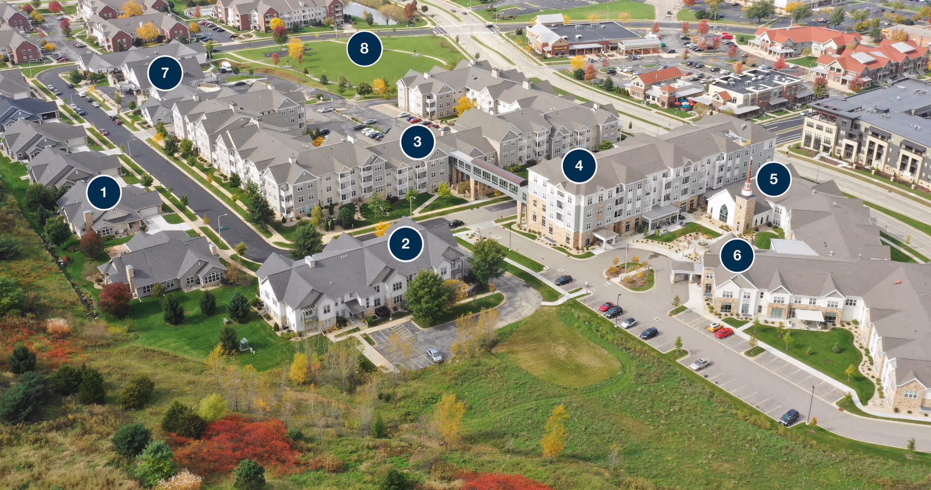Aerial view of All Saints Neighborhood senior living facility showing multiple residential buildings, parking areas, green spaces, and roads within the complex.