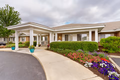 Cobblestone Manor assisted living facility entrance with a white canopy and landscaped front garden.