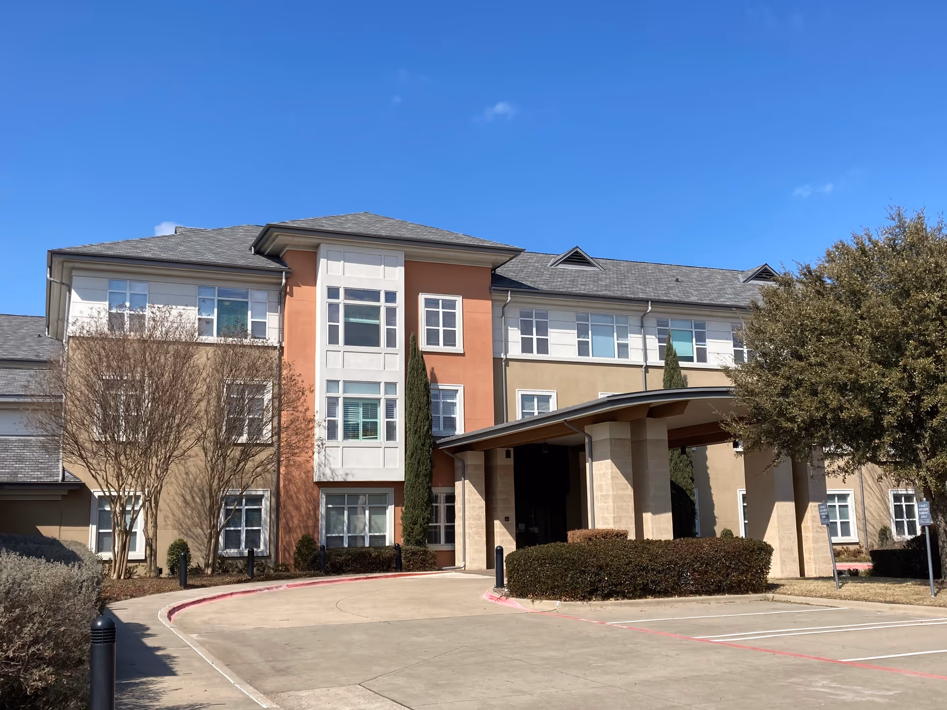 Three-story senior living building with a covered entrance and surrounding shrubs.