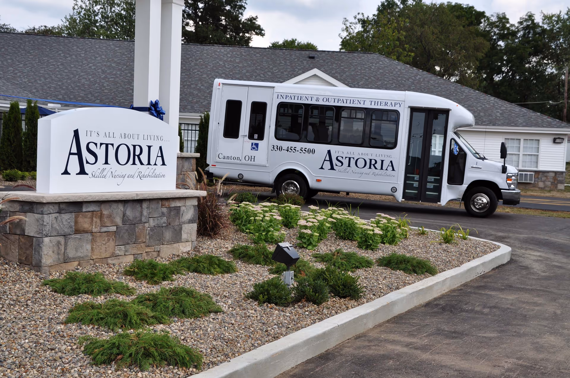 View of Astoria facility entrance with a branded shuttle bus and landscaped front yard.