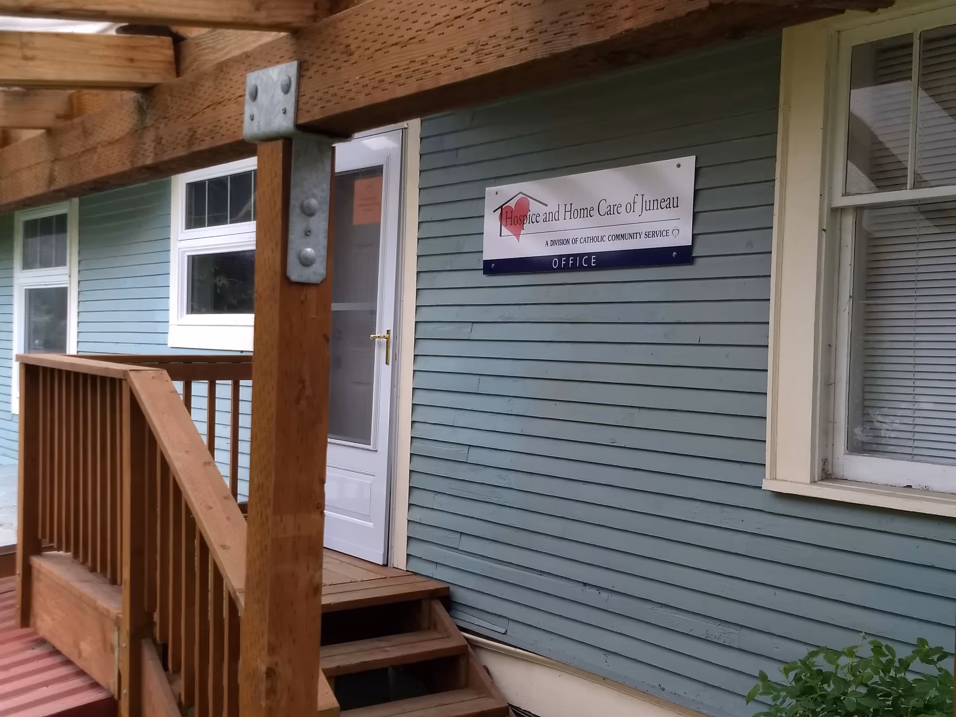 Exterior view of a blue house with a wooden porch and Hospice and Home Care sign.