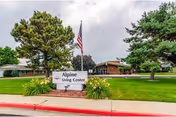 Exterior view of a senior living center with a sign, flag, trees, and lawn.
