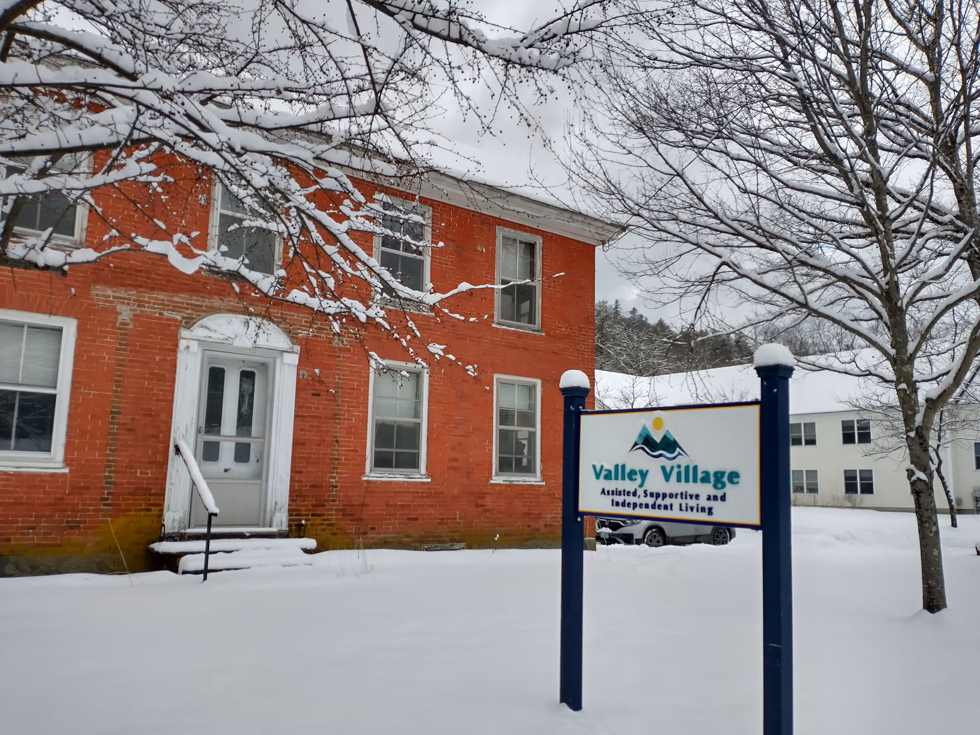 Red brick senior living building with snow and a blue-framed Valley Village sign.