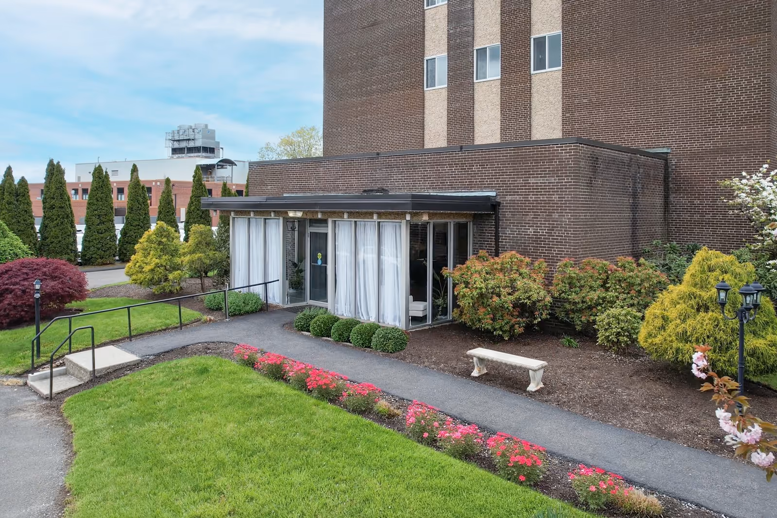 Exterior view of a brick facility entrance with glass doors and landscaped walkway.