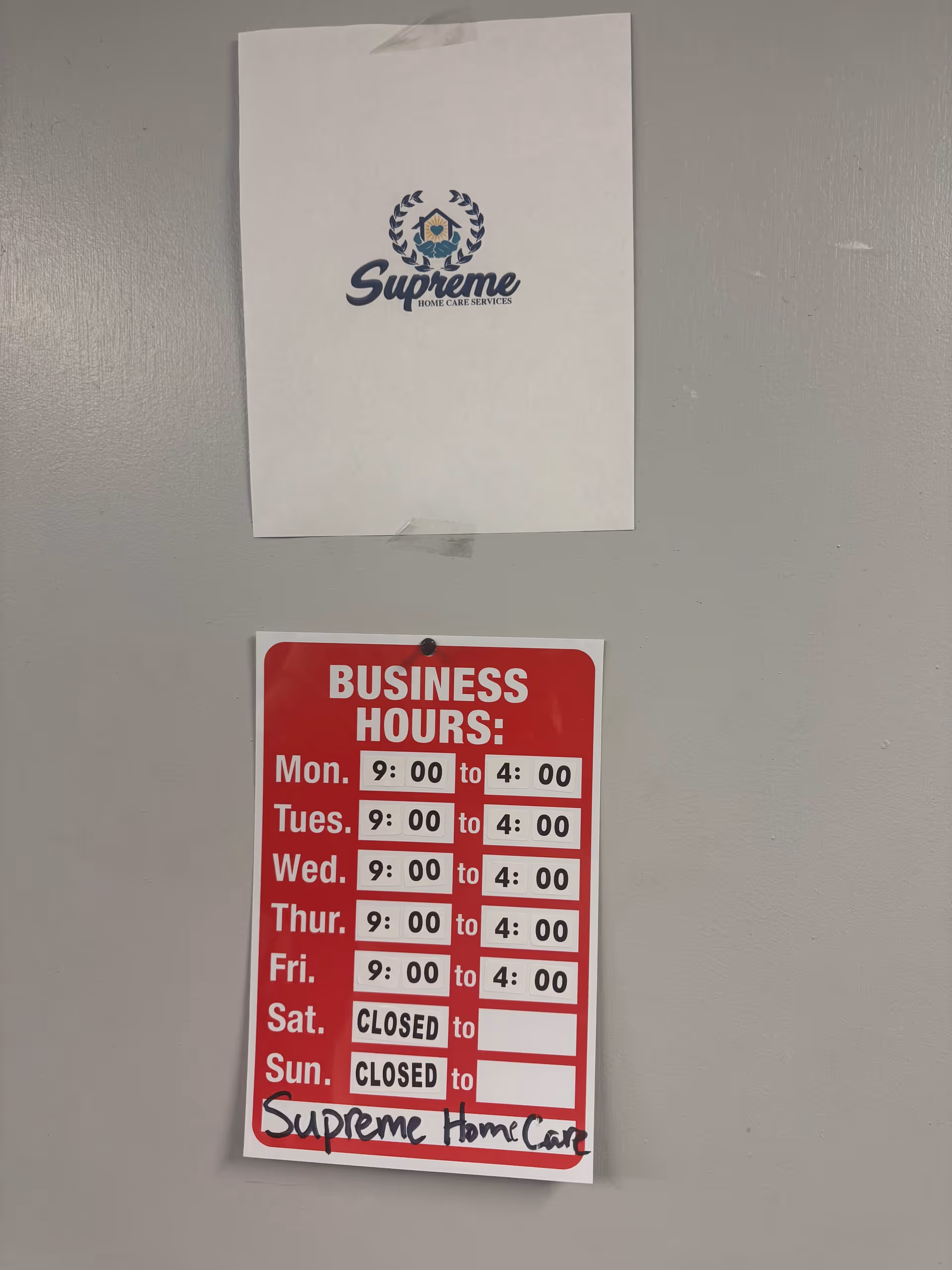 Two posters on a gray wall: a Supreme Home Care Services logo and business hours sign.