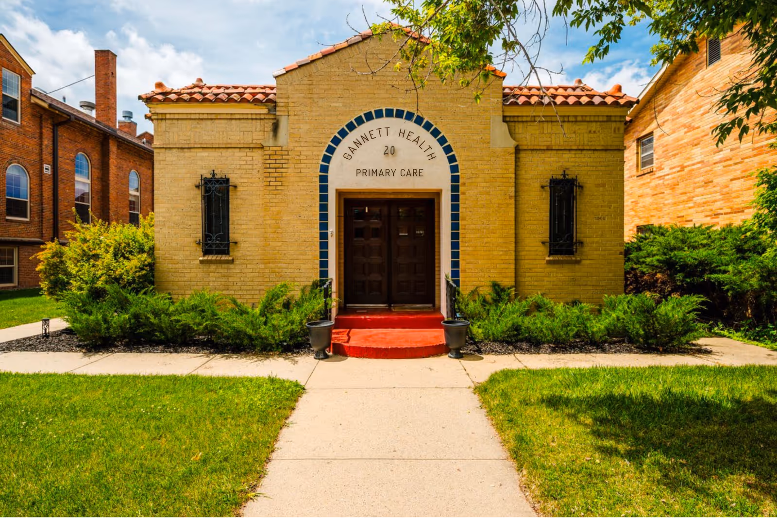 Brick building with blue-trim arch entrance reading Gannett Health Primary Care and red steps.