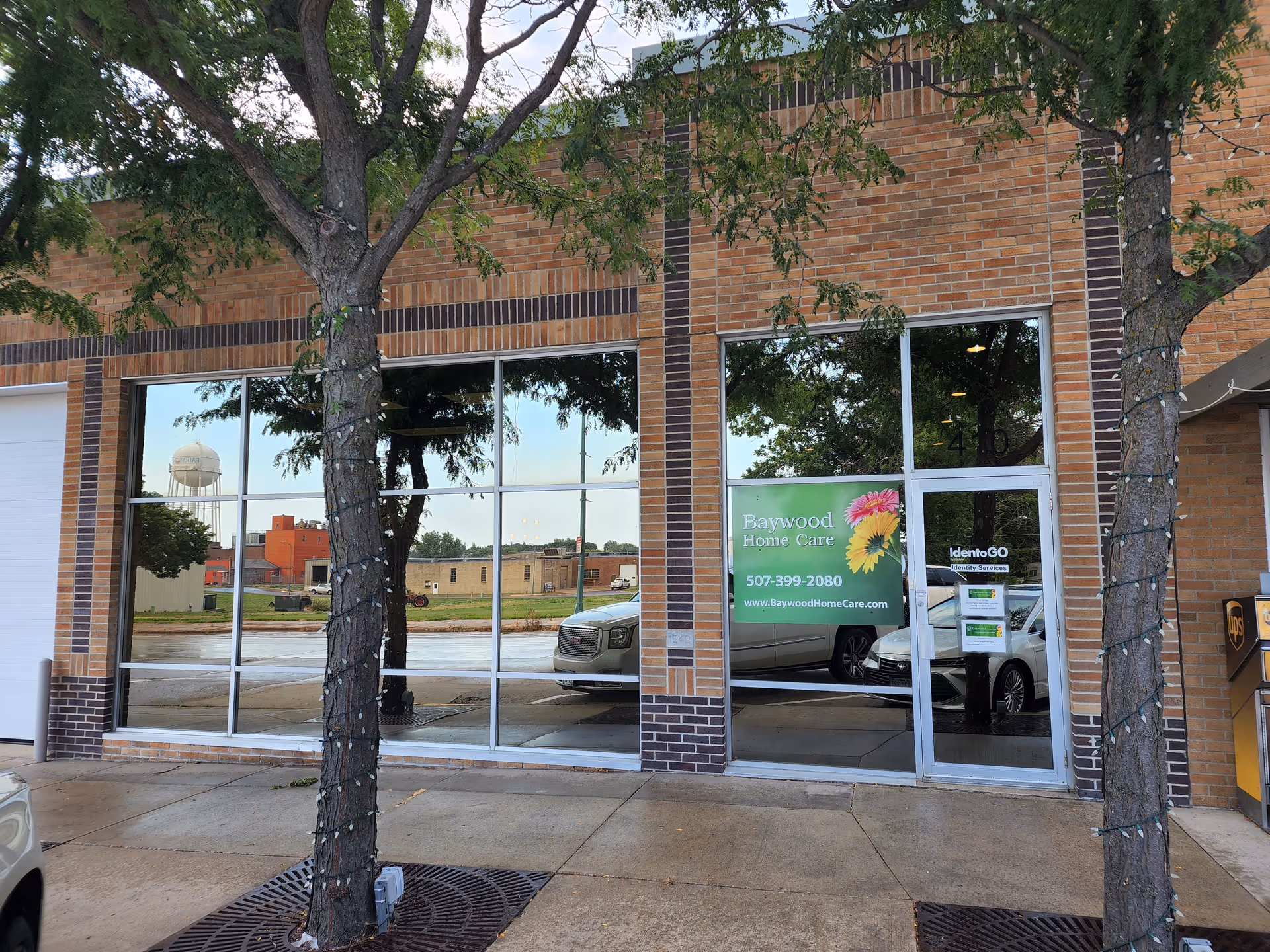 Brick storefront with large windows, Baywood Home Care sign, and two trees in foreground.