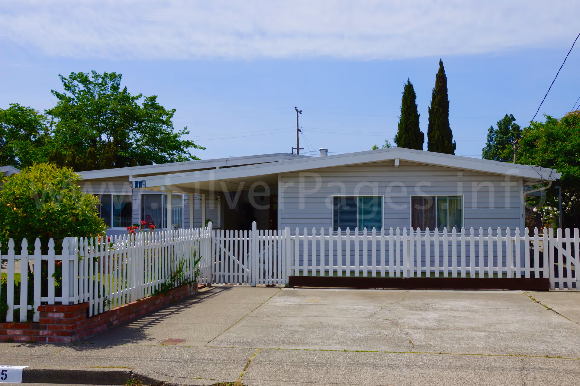 Single-story light gray building with white picket fence and driveway.