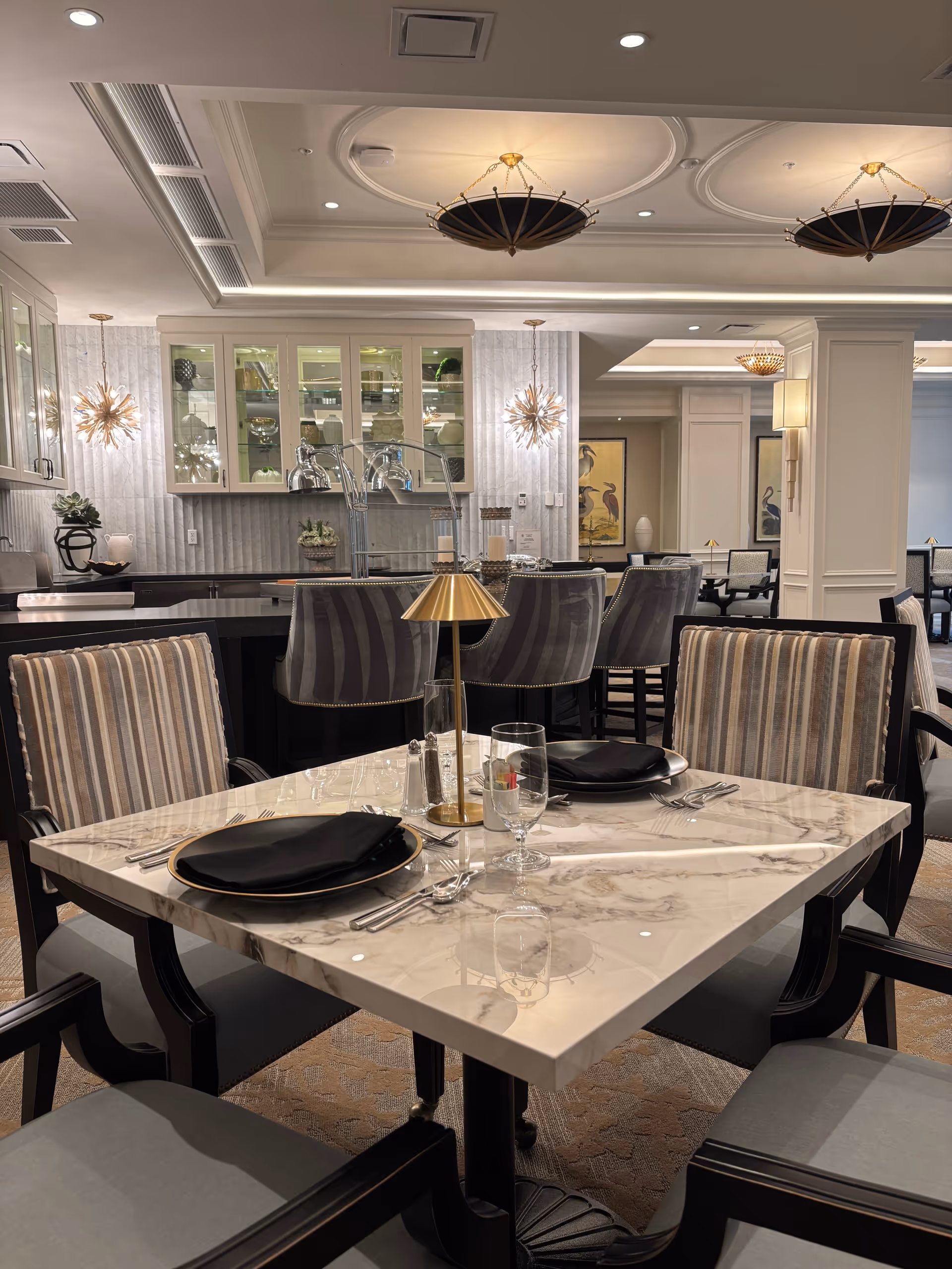 Elegant dining area with marble table, striped chairs, and a bar in the background.