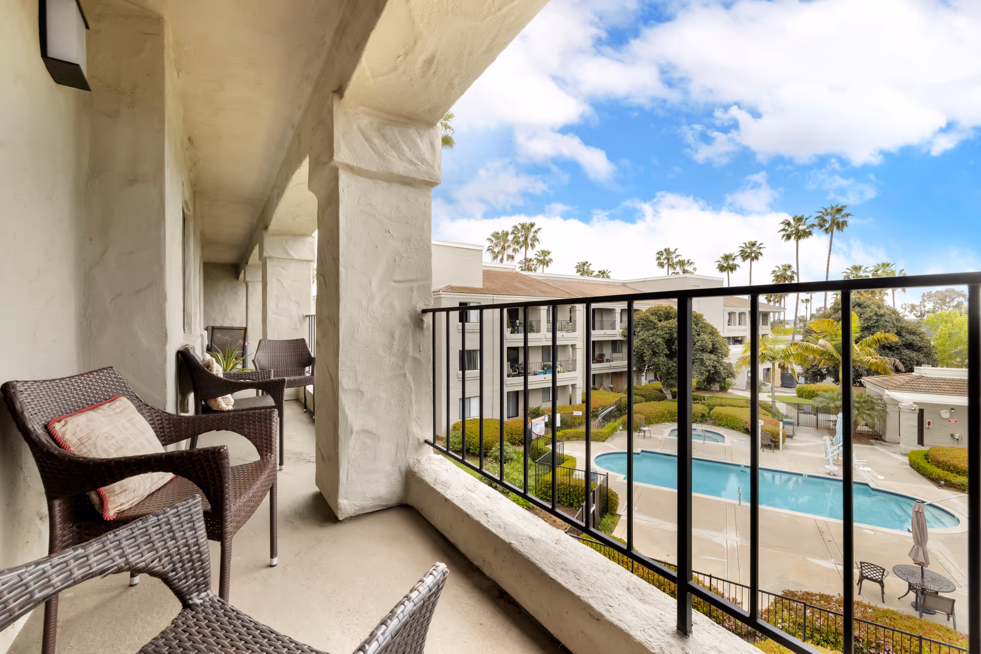 Patio seating on a balcony overlooking a pool and palm trees at Laguna Estates Senior Living.