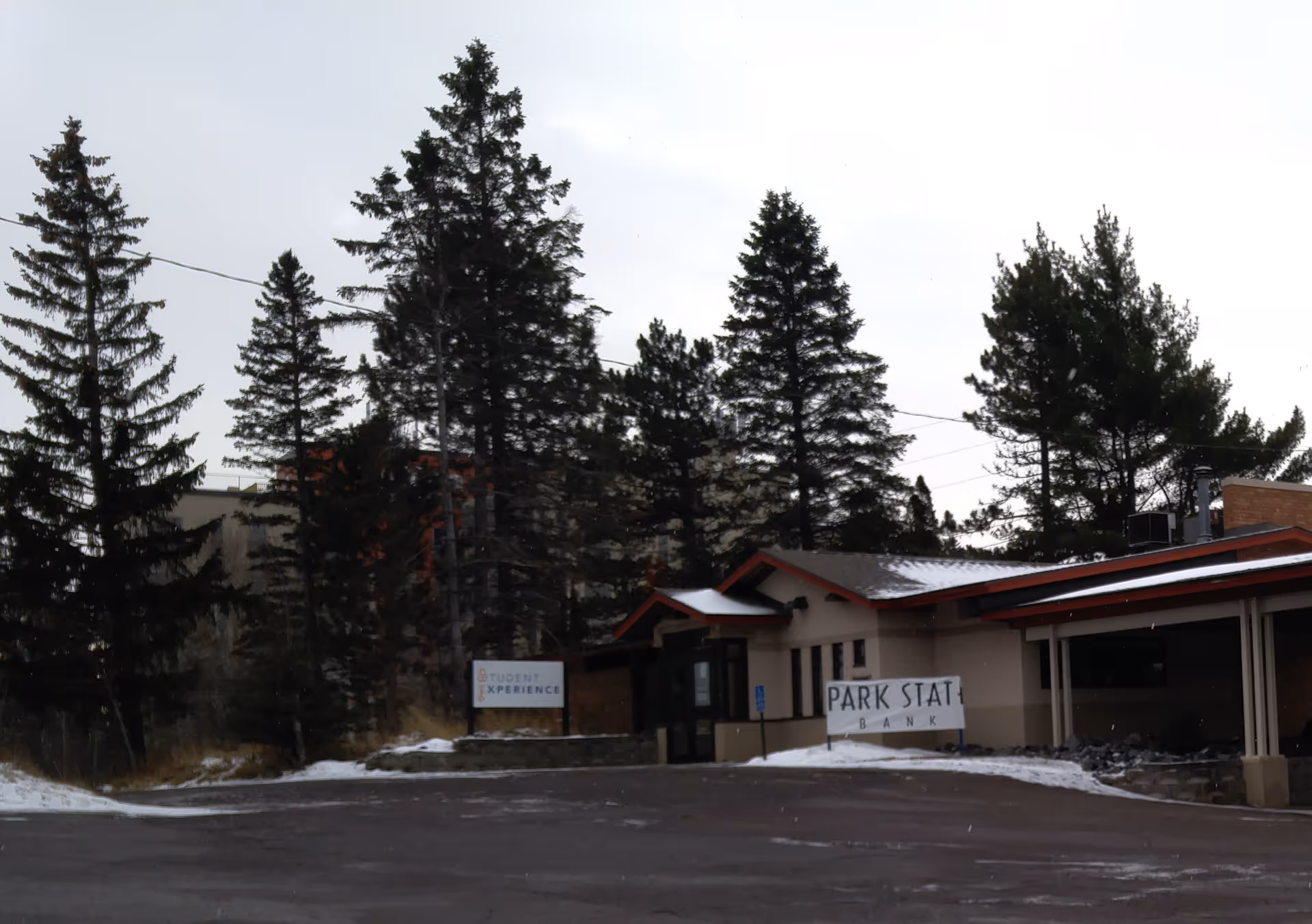 Exterior view of a low, red-roofed facility labeled Student Experience with snow