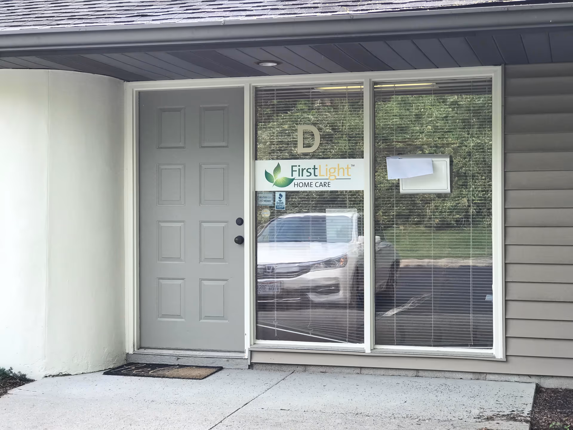 A facility entrance with a gray door and window displaying FirstLight Home Care signage.