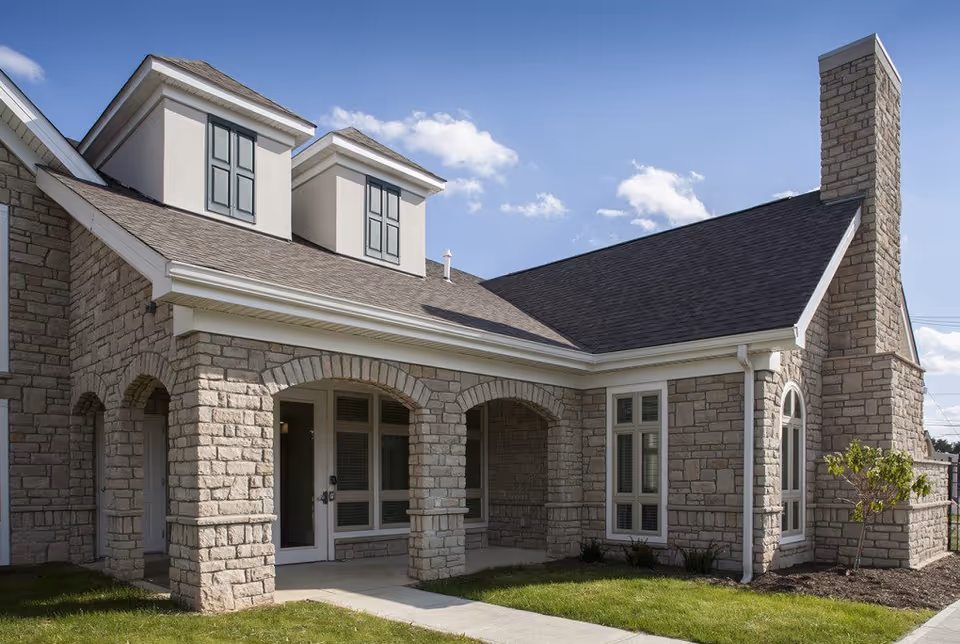 Stone exterior of a senior living facility with arches, windows, and a chimney under blue sky.