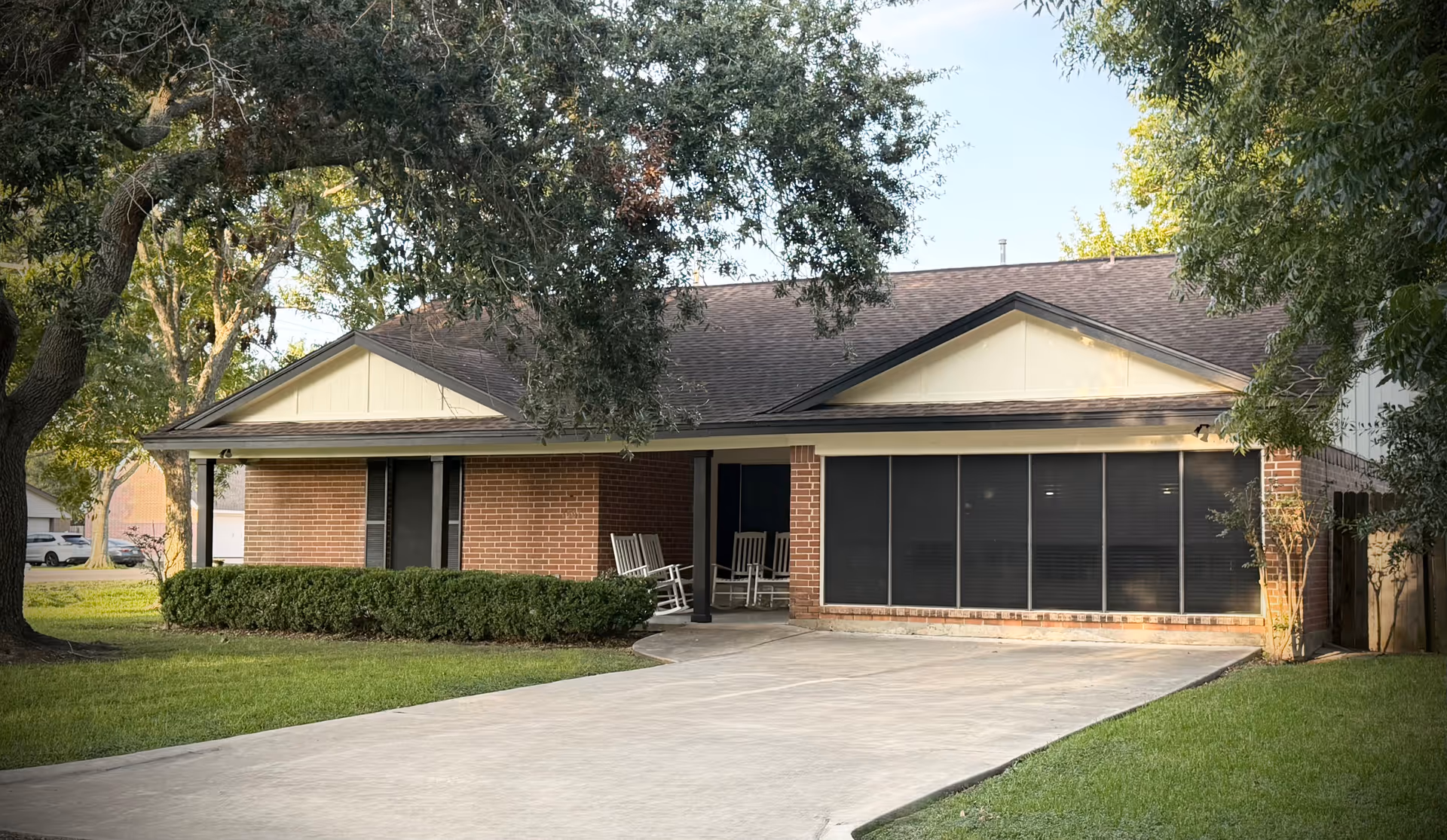 Single-story brick assisted living facility exterior with a curved driveway, front porch seating, and shaded entrance.