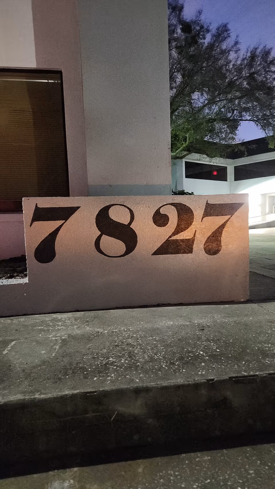Exterior wall with large numbers 7827 and building entrance in twilight.