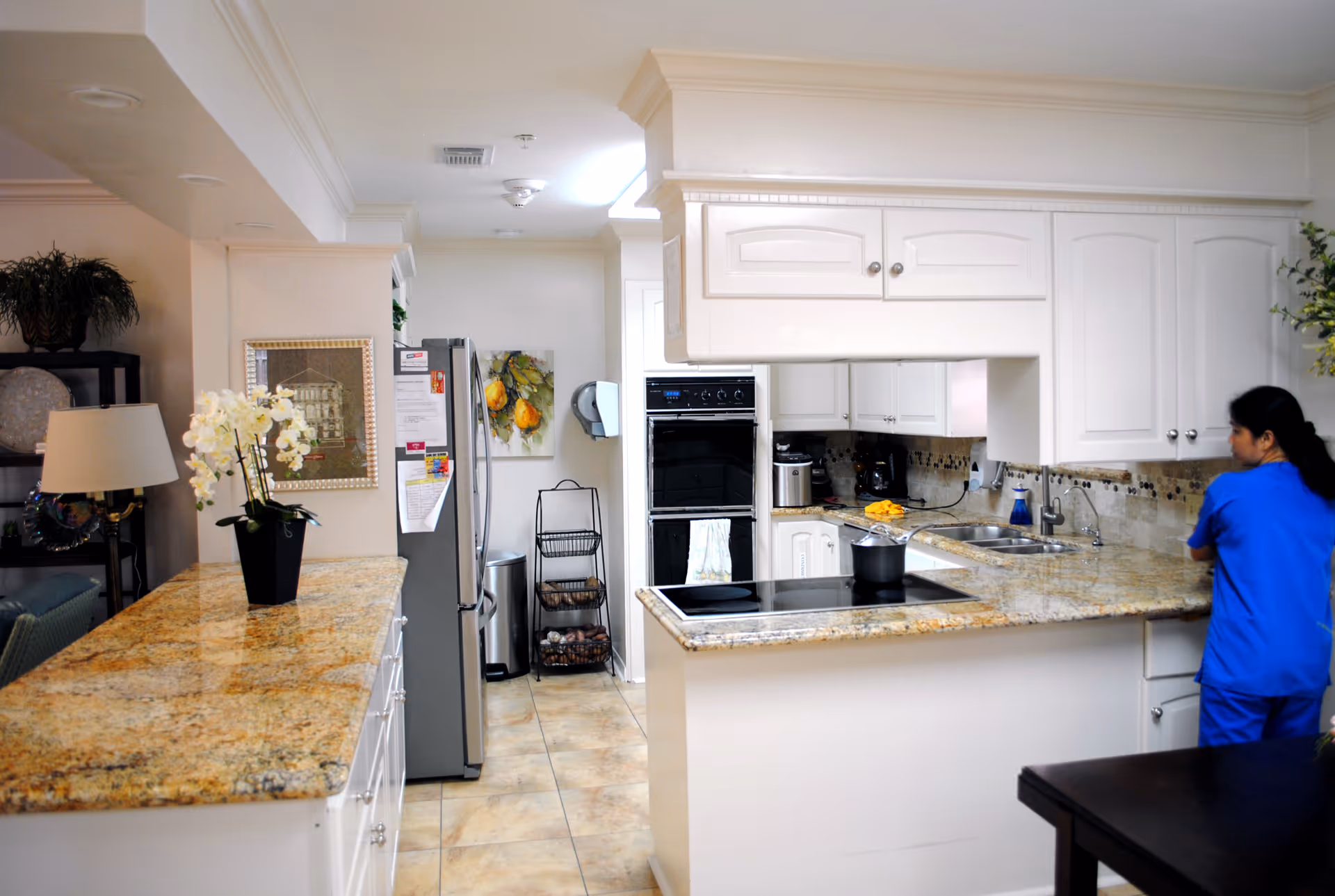 White kitchen with granite countertops and a caregiver in blue scrubs at the counter