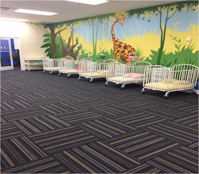 Interior room with a row of white cribs beside a jungle-themed wall mural.