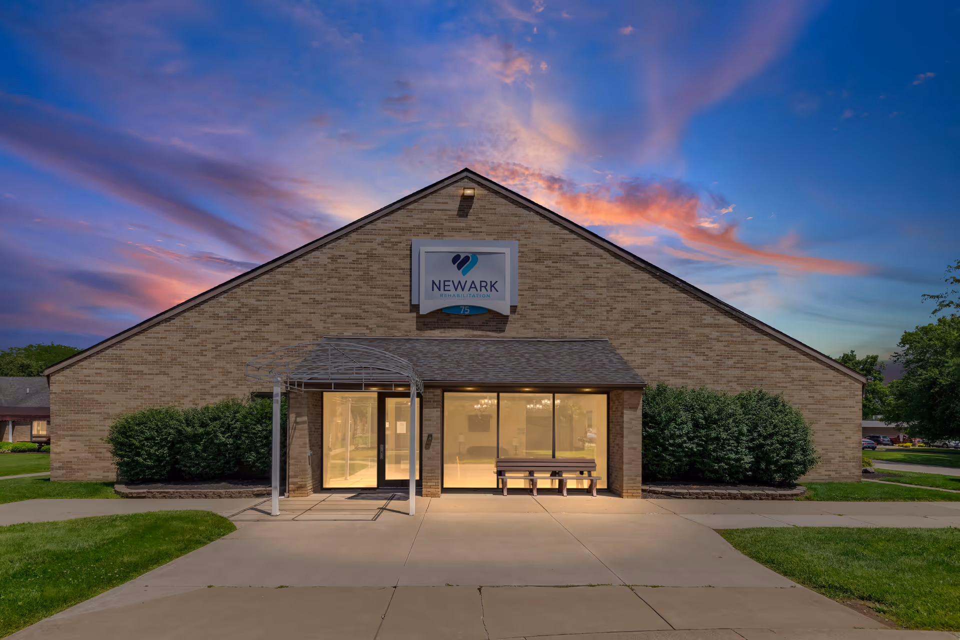 Brick building with Newark Rehabilitation sign, glass doors, walkway, and sunset sky.