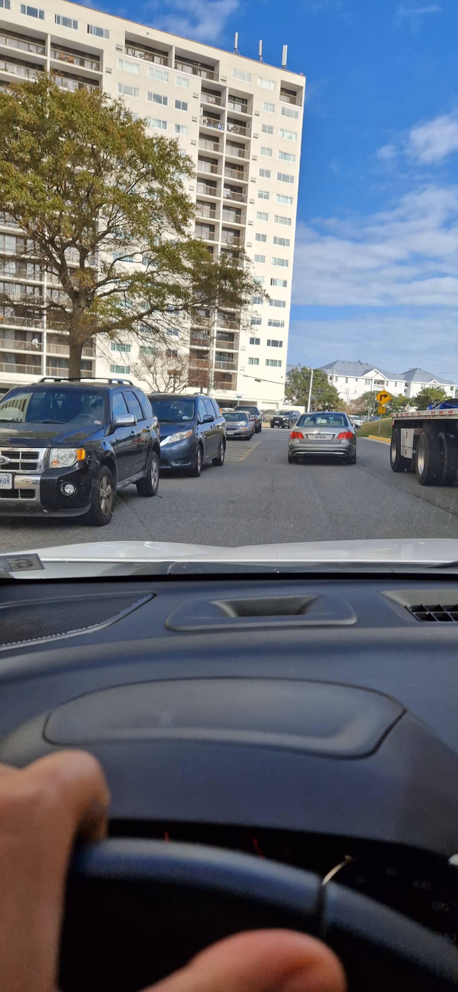 From inside a car, view of a tall senior living building exterior with parked cars.