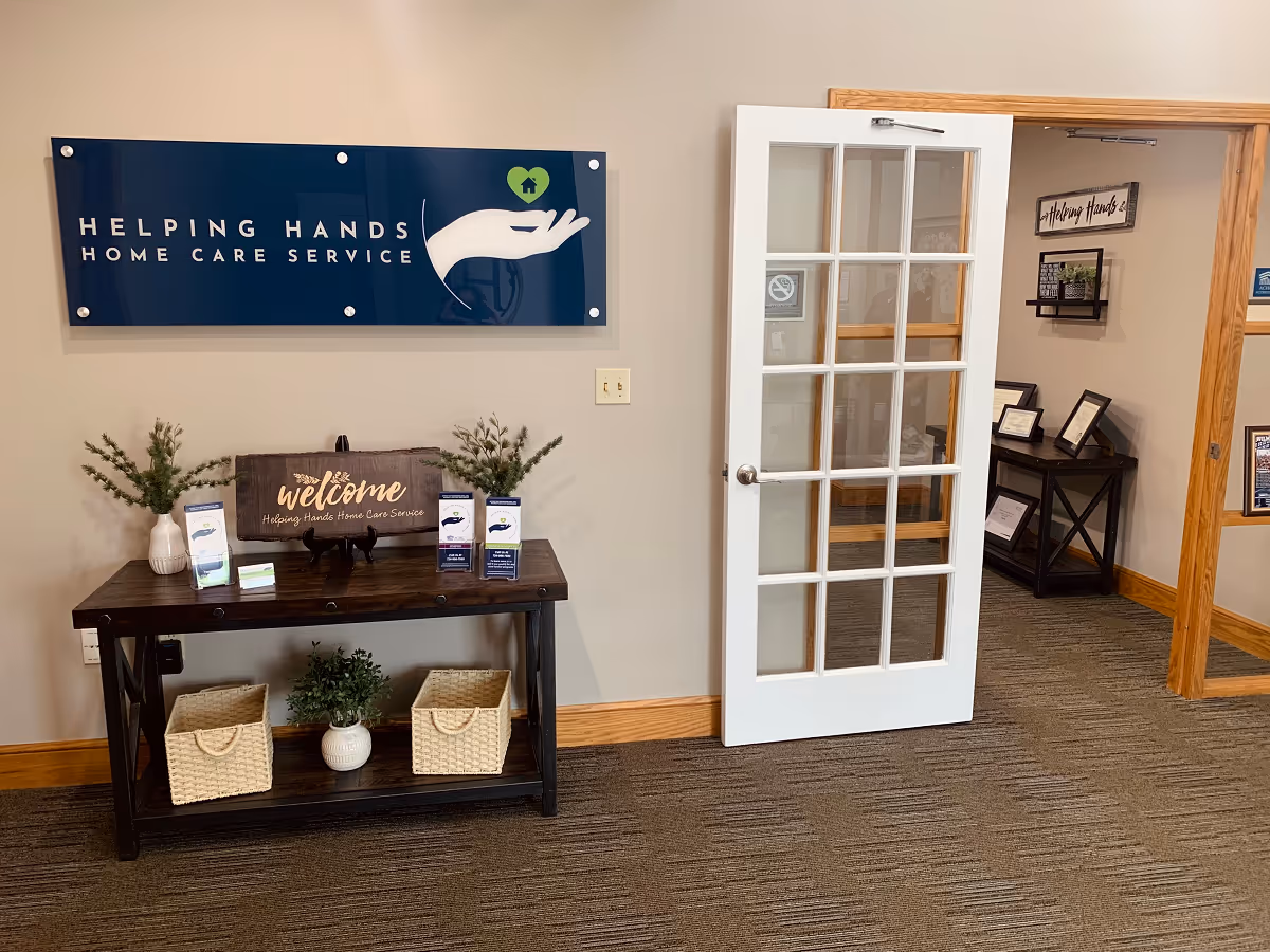 Interior reception area with Helping Hands sign, welcome table, brochures, and glass door.