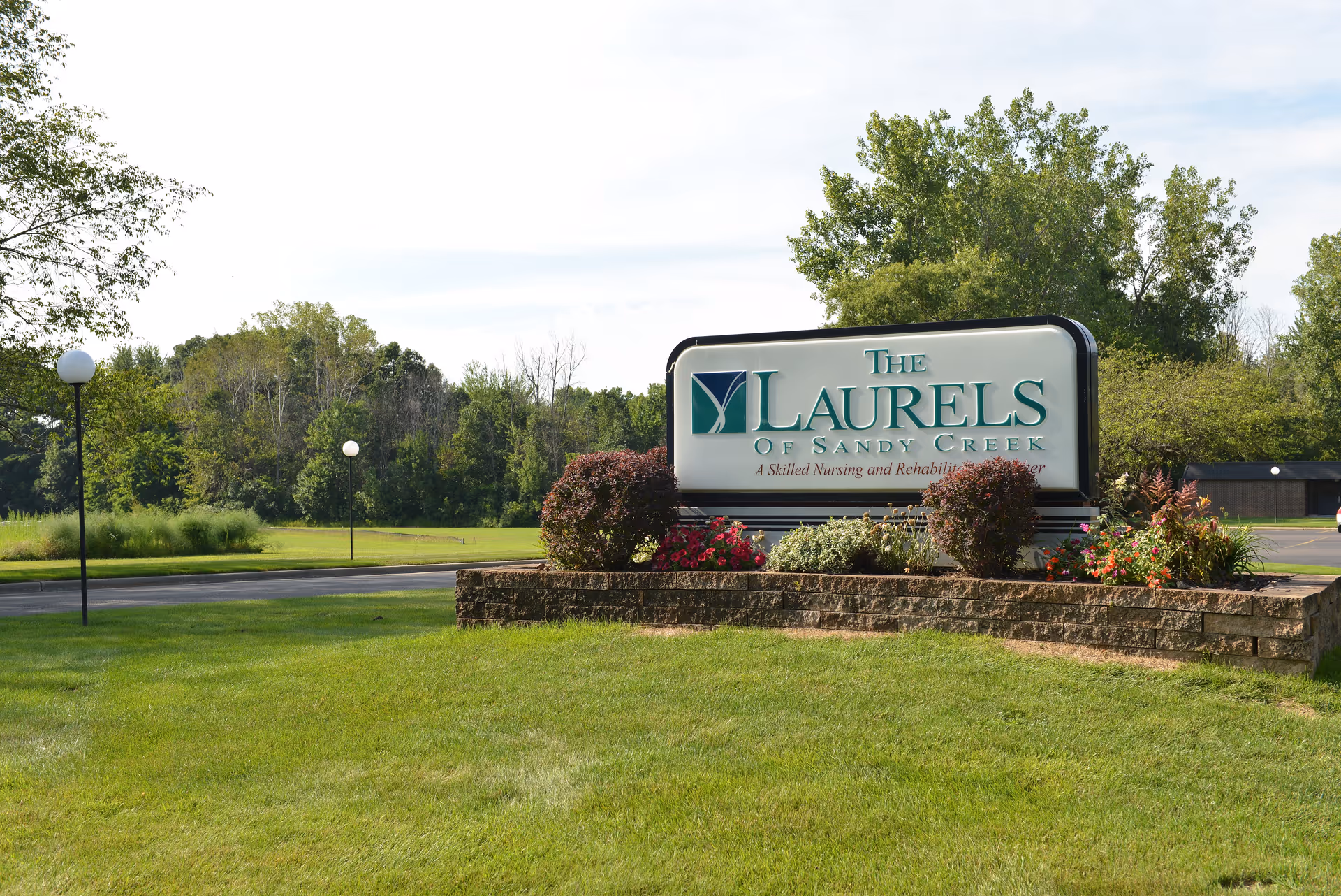 A well-kept lawn surrounds a large sign for The Laurels of Sandy Creek.