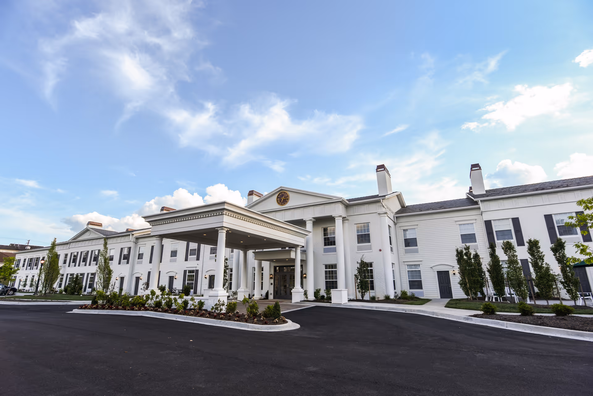 Exterior view of a white, columned senior living building with a covered entrance and circular driveway.