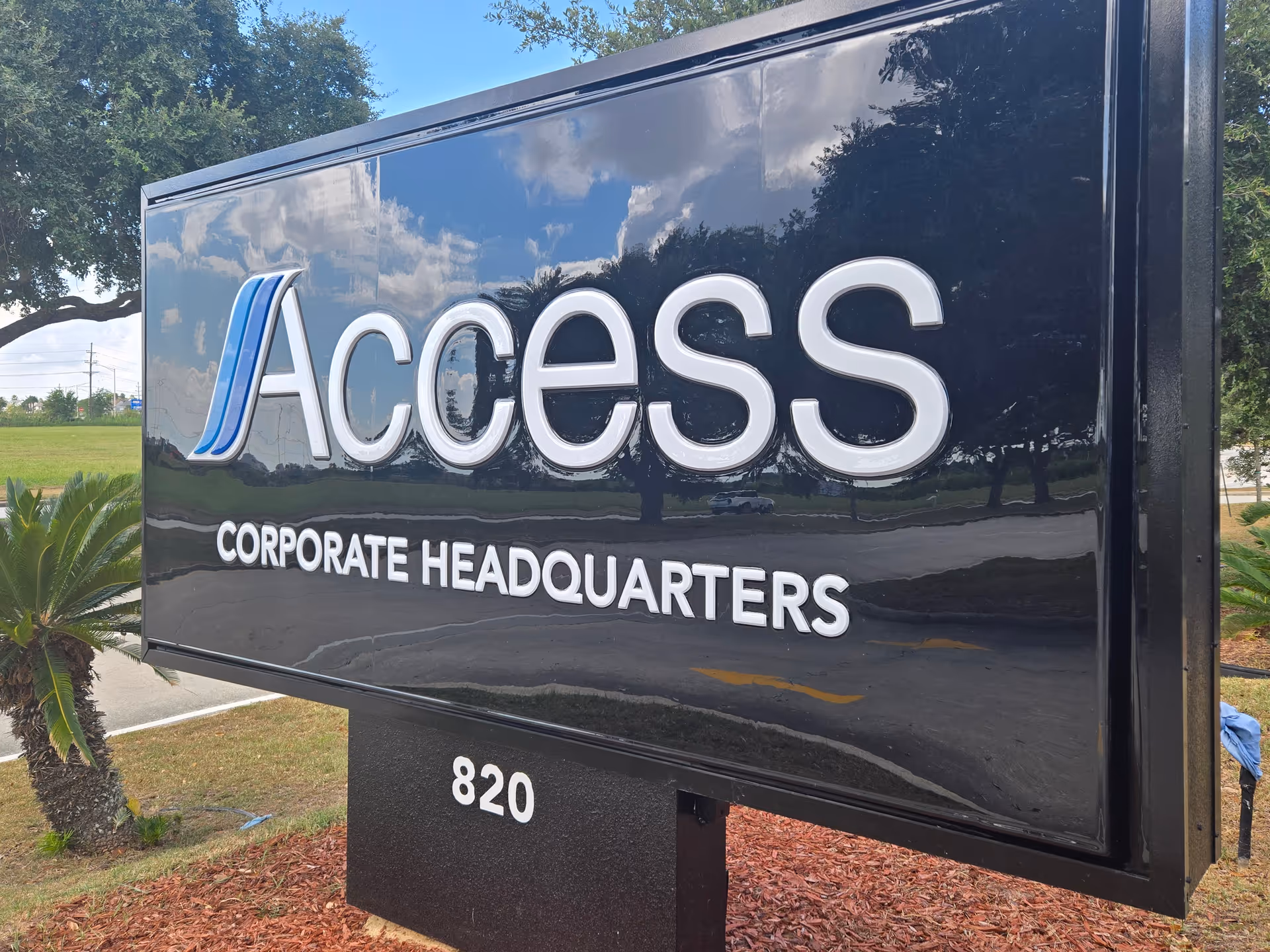 Large black outdoor sign reads 'Access Corporate Headquarters' with trees and landscaping nearby.