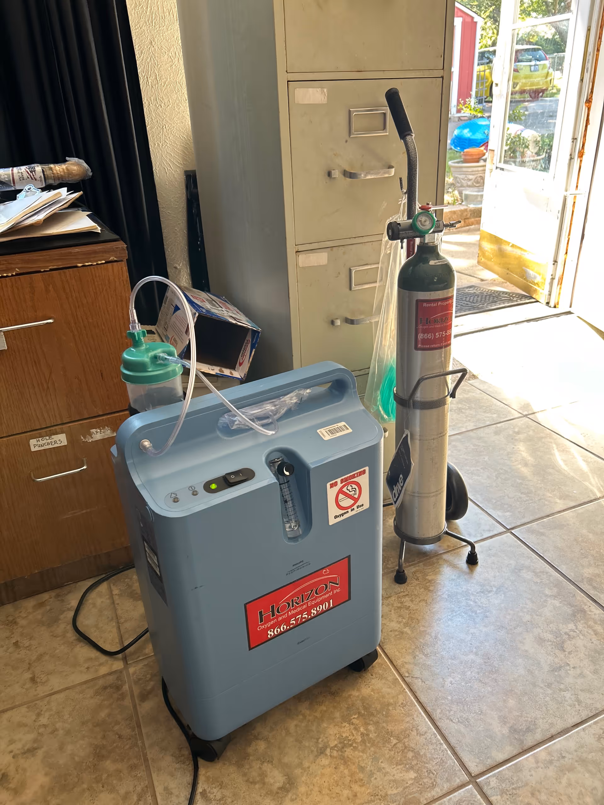 Medical oxygen equipment and a blue oxygen concentrator in a tiled interior corner.