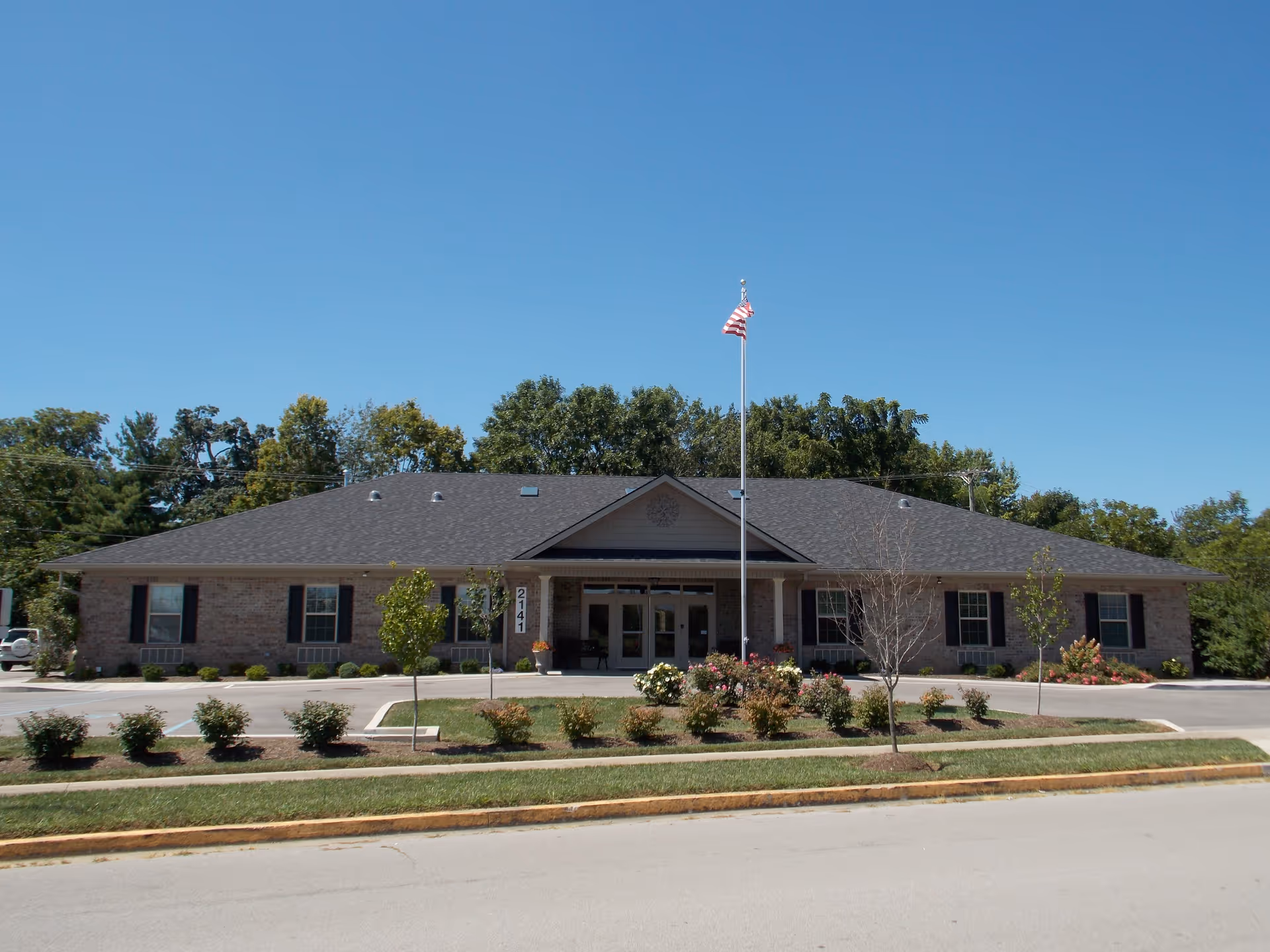 Single-story brick assisted living facility with a flagpole and landscaped front lawn.