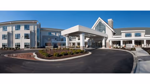 Large modern senior living center exterior with driveway, porte-cochere, and landscaped circular drive.