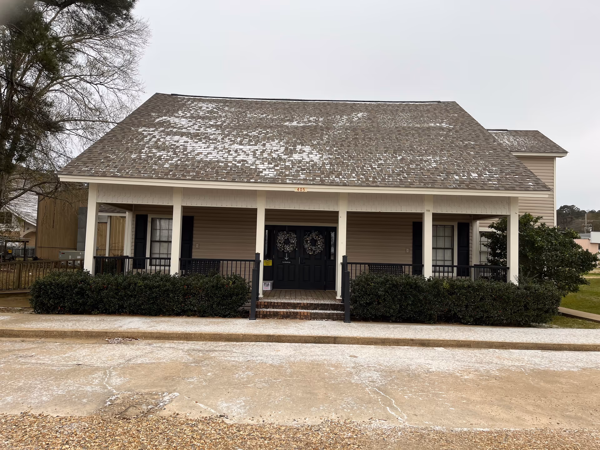Front view of a single-story building with a covered porch, double doors, and surrounding shrubs.