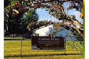 Front yard scene with Caring Acres Nursing and Rehab sign, a fence, and building in background.