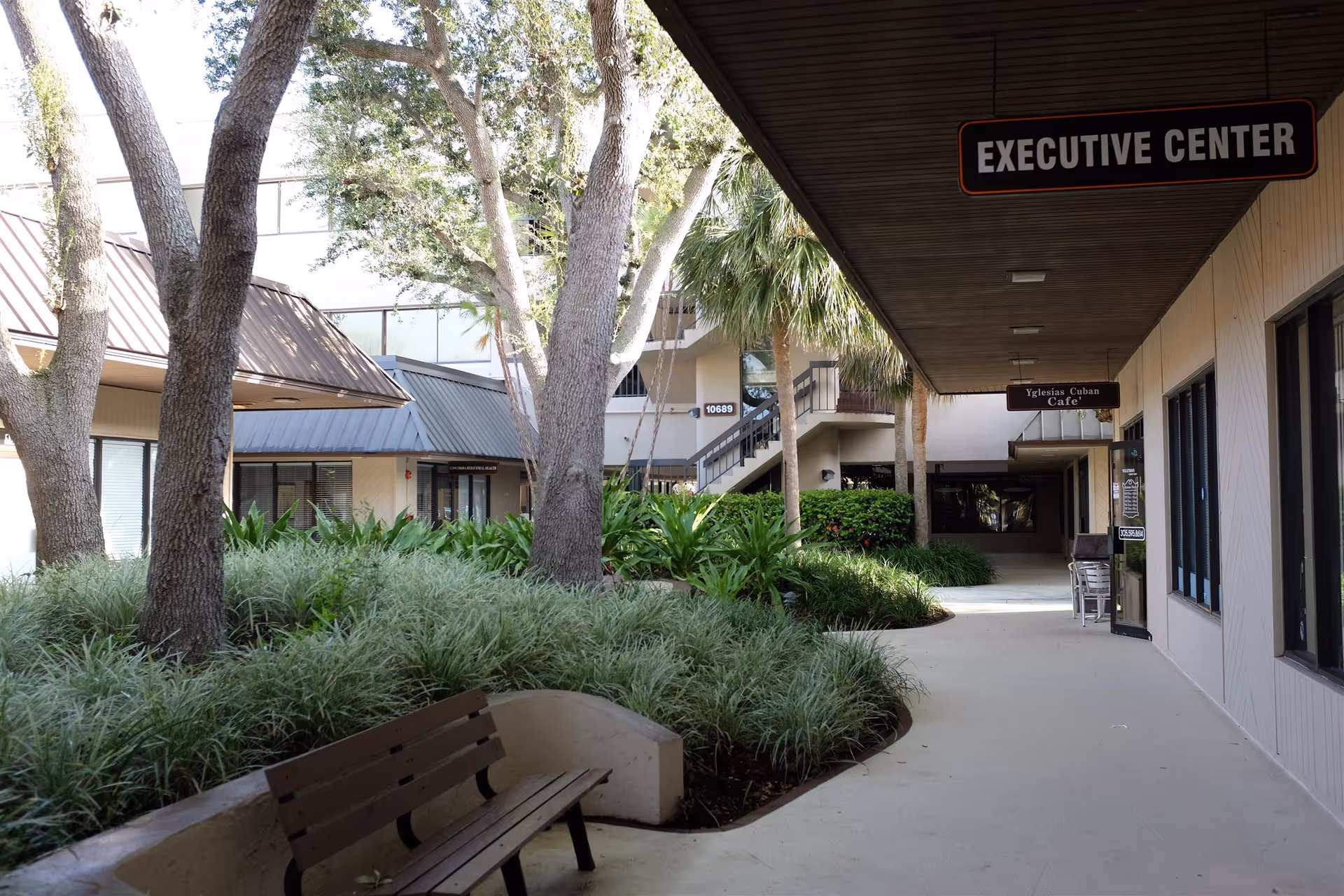 Outdoor walkway at a senior living campus with benches, trees, and landscaped greenery.