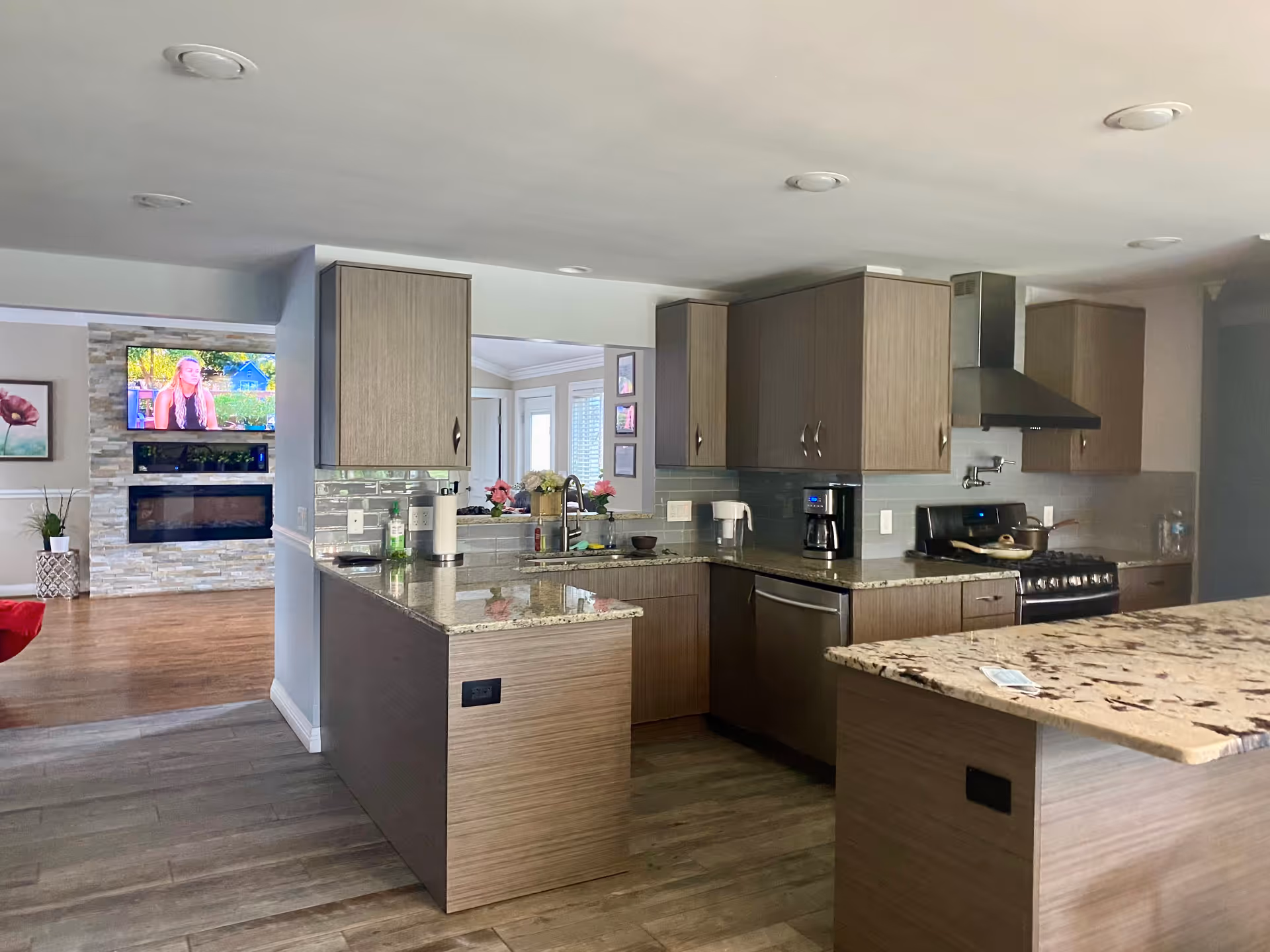 Modern kitchen with island, granite countertops, wood cabinets, and stainless appliances in an open-plan layout.
