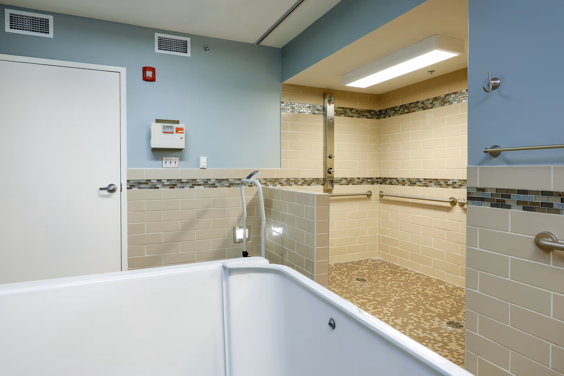 Accessible bathroom featuring a large tub, beige tiles, and grab bars.