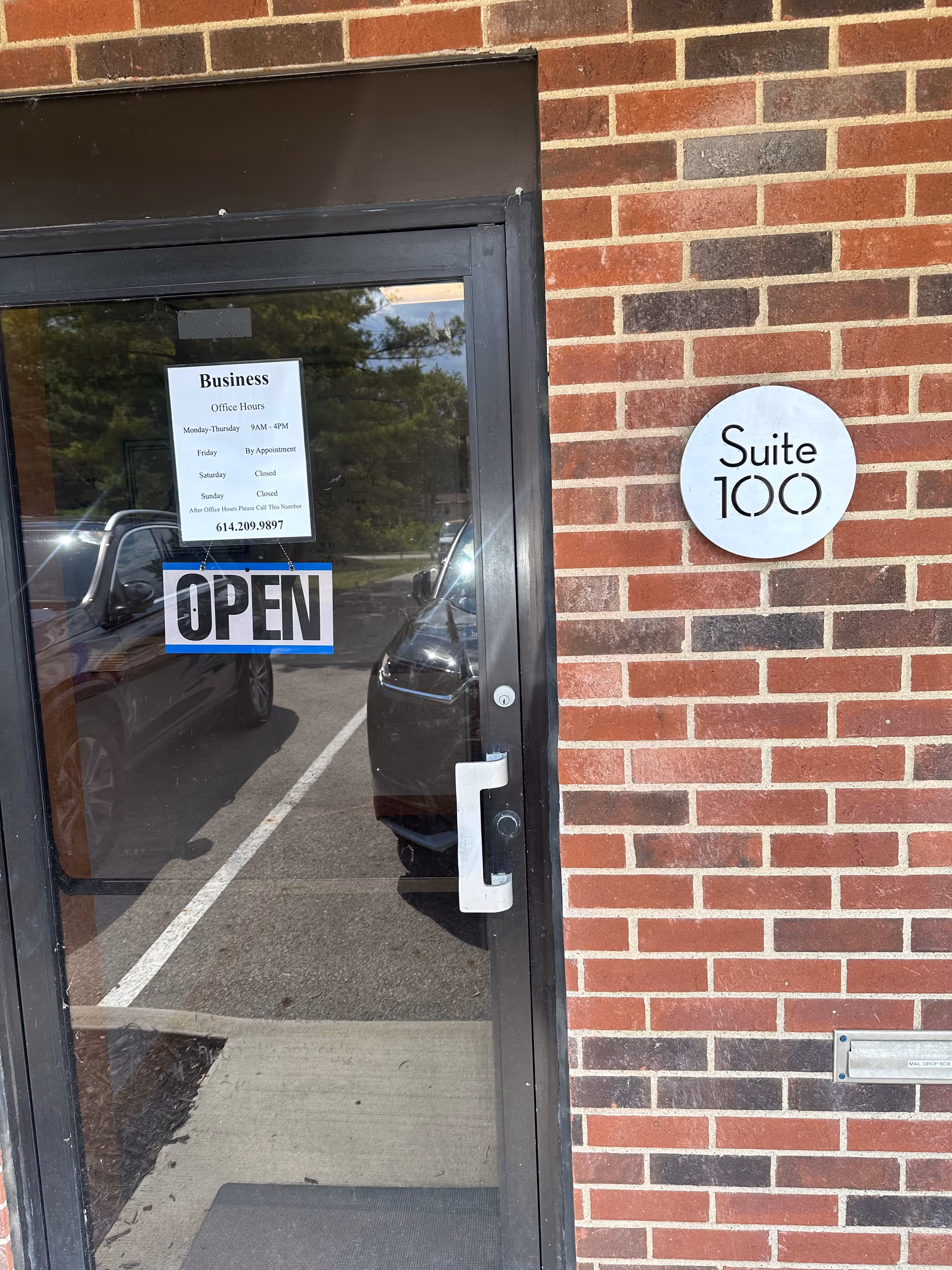 Brick exterior entrance with glass door labeled Suite 100 and an OPEN sign.