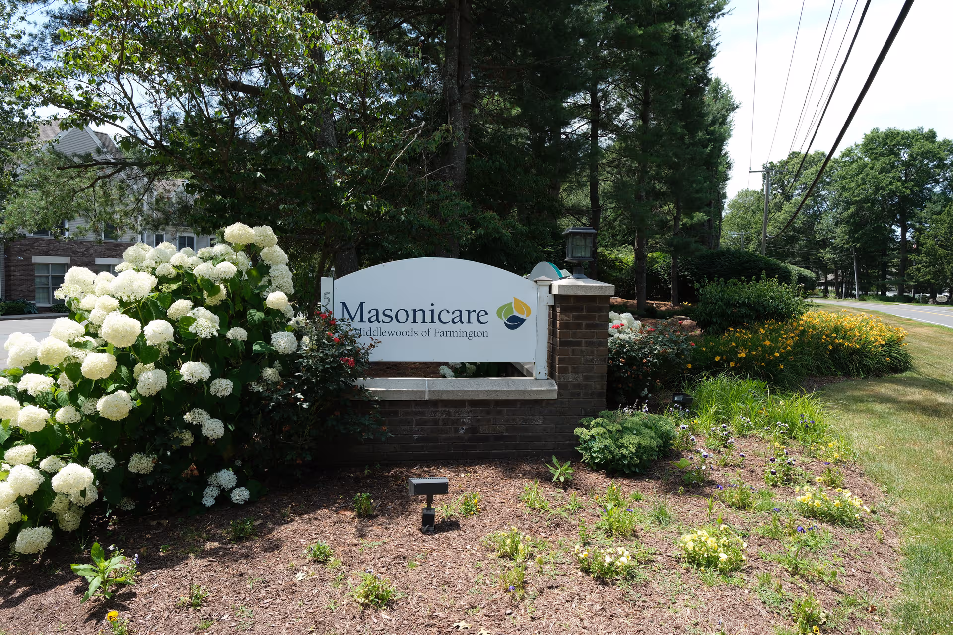 Exterior view of the Masonicare at Middlewoods of Farmington entrance with flowering shrubs.