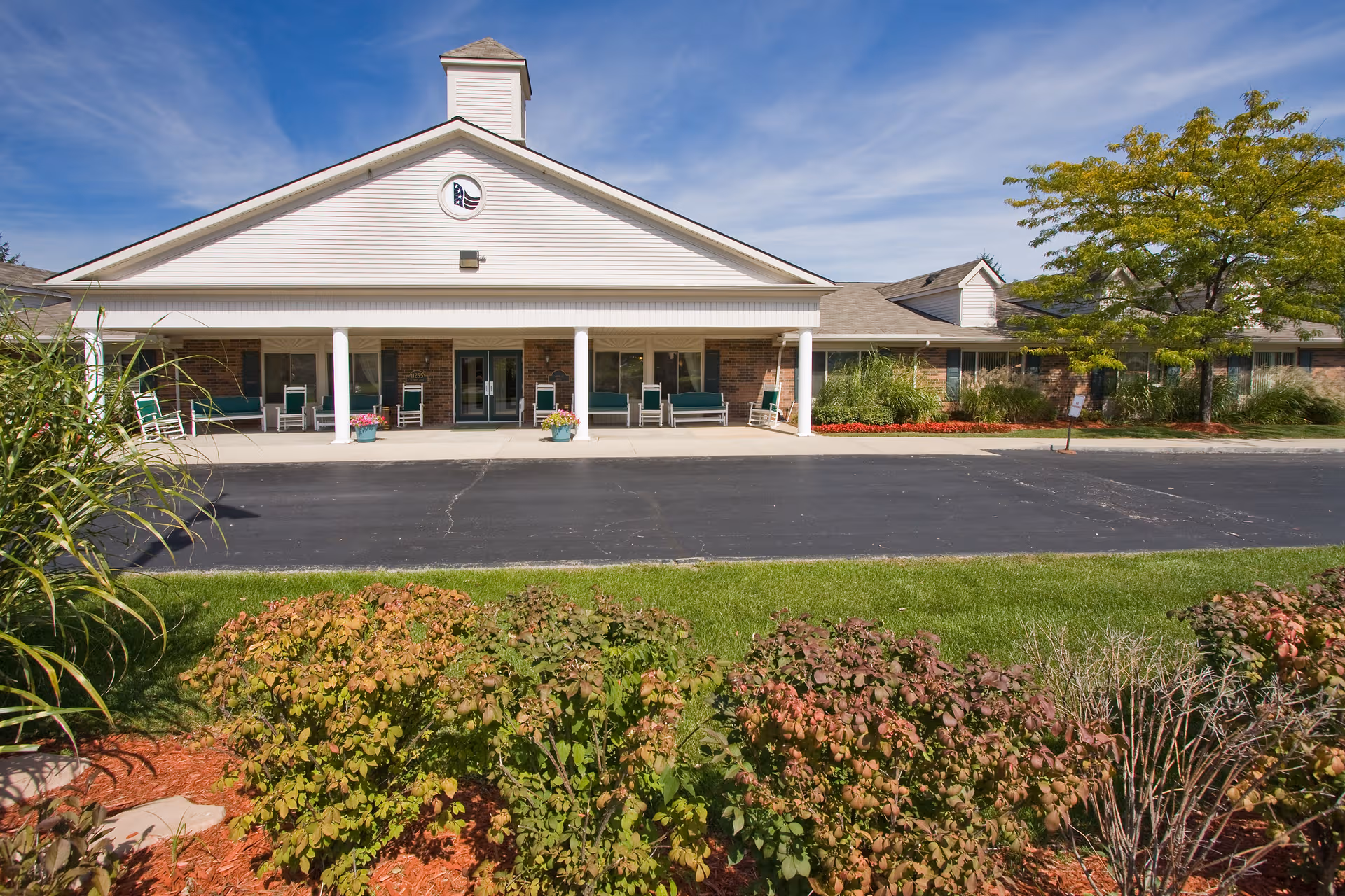 Single-story building entrance with a covered porch, benches, and well-kept landscaping.