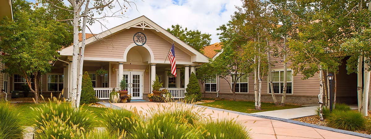 A senior living facility building with a covered entrance, flag, and landscaped front yard
