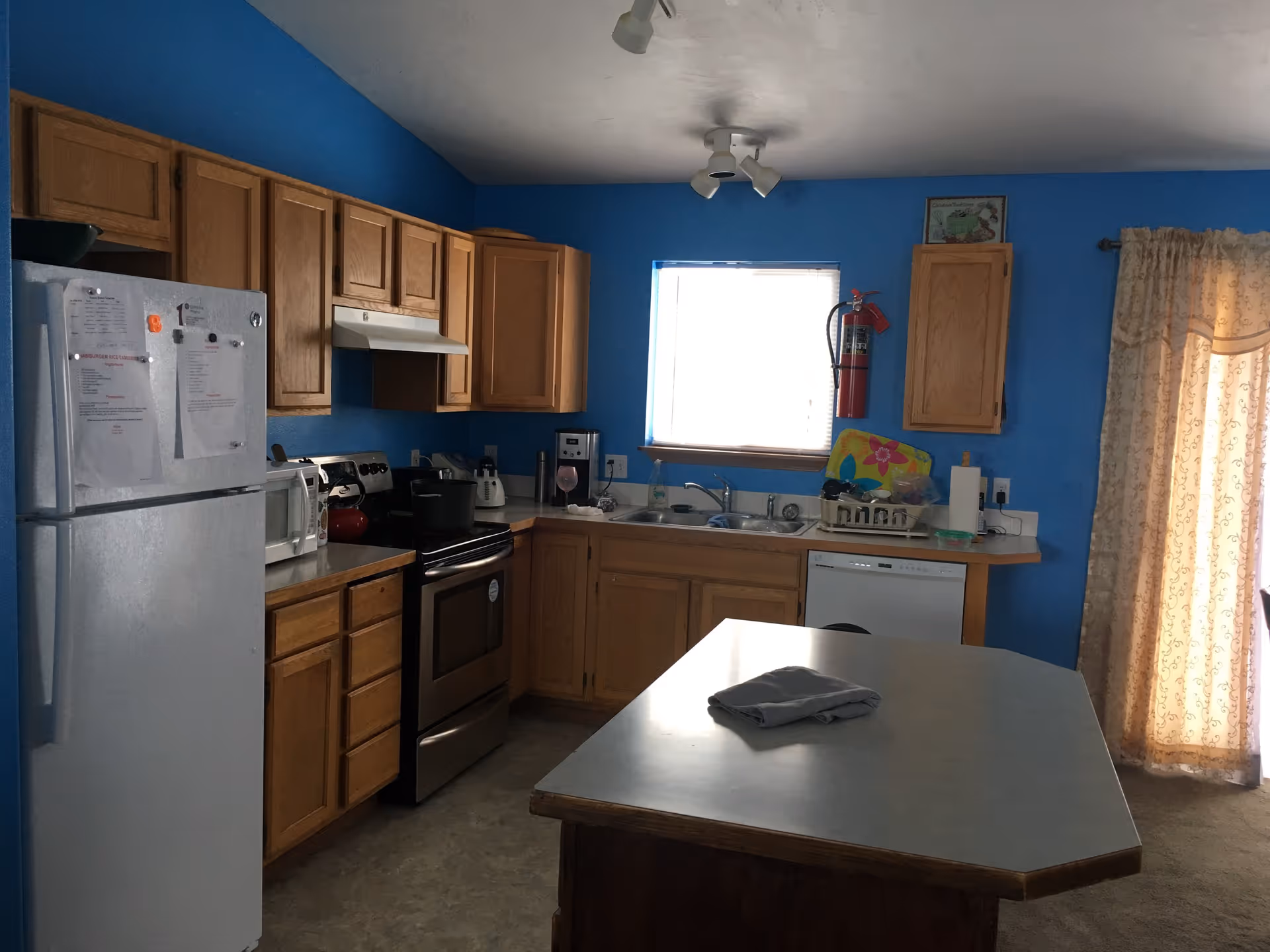 Blue kitchen with wooden cabinets, stainless appliances, and a central island.