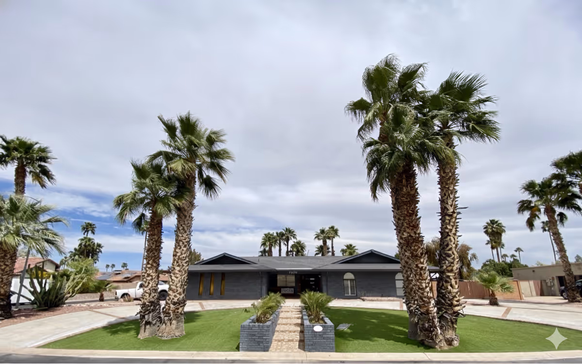 Single-story senior living facility with palm trees, a central entrance, and a paved front.